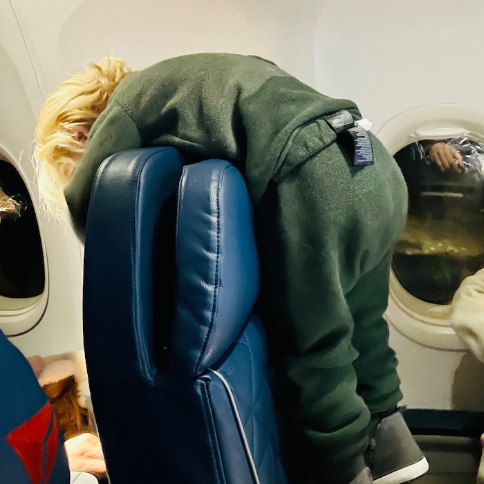 Toddler hanging over plane seat back 