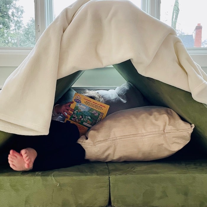 Toddler reading in a fort